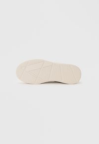 Semelle de chaussure en caoutchouc beige avec motifs géométriques et adhérence texturée sur fond blanc uni.