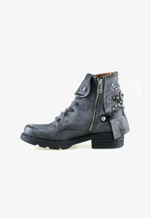 Donkergrijze leren enkellaars met zijrits, veters aan de voorkant, decoratieve metalen studs en een kleine gestapelde hak tegen een witte achtergrond.