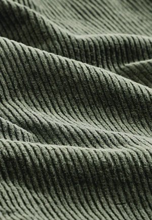 Il tessuto di corduroy verde presenta prominenti strisce verticali, conferendogli un aspetto texture con una finitura morbida e pelosa.