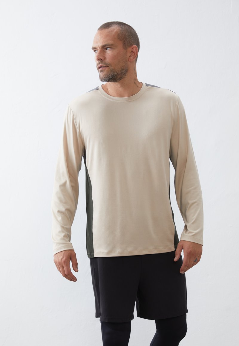 Beige langekorte mouwen shirt met donkergroene zijpanelen; gladde textuur, ronde hals en ingezette mouwen. Gemaakt met zwarte shorts.