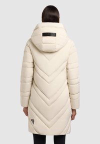 Giacca puffa crema con cuciture a maglia a V, un grande cappuccio e accentuazioni nere del logo. Texture liscia e imbottita con taglio lunghezza ginocchio.