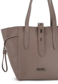Torebka typu tote z taupe'owej skóry o strukturalnym kształcie, z dwoma uchwytami i detalem w postaci paska na przodzie. Posiada wytłoczone logo "Venezia" na dole.