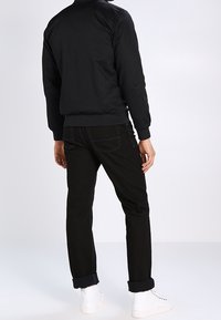 Giacca bomber nera con una texture liscia, caratterizzata da polsini elasticizzati. Abbinata a pantaloni in denim nero con risvolti e sneaker bianche.