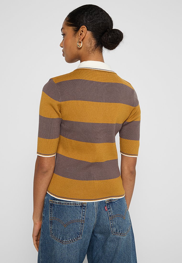 Polo de manga corta y canalé en rayas mostaza y marrón, con cuello y puños blancos, combinado con jeans de denim de talle alto.