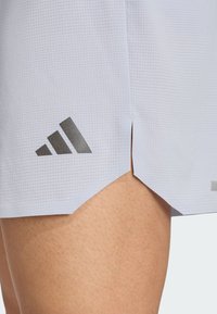 Hellgraue Sportshorts mit einem strukturierten Muster, ausgestattet mit einem seitlichen Schlitz und einem dunkelgrauen adidas-Logo nahe dem Saum.