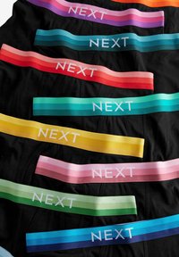Sous-vêtements noirs variés avec des élastiques colorés arborant le logo "NEXT" en blanc. Les élastiques sont de couleurs dégradées : violet, bleu, vert, jaune, rose, orange et rouge.