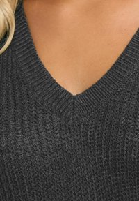 Dunkelgrauer Strickpullover mit V-Ausschnitt, geripptem Muster und einer Nahaufnahme, die die Dicke des Stoffes betont.