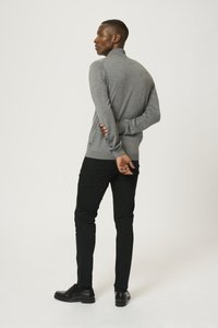 Grå långärmad tröja med hög krage, bärs med svarta slim-fit-byxor och svarta skor. Tröjan har ett strukturerat stickat mönster.