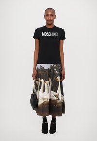 Melnā T-kreklā ar "MOSCHINO" logo, apvienots ar garu svārku, uz kura ir balto zīļu prints, nēsā melnas augstas papēžu potīšu kurpes un rokassomu.