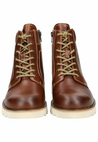 Botas de cuero marrón hasta el tobillo con cordones en tono dorado, costuras decorativas, cremalleras laterales y suelas de goma en color blanco roto. Diseño de punta redondeada y plana.