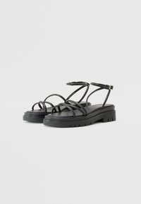 Sandales noires à brides avec une semelle épaisse, dotées de plusieurs fines brides et d'une fermeture à boucle, fabriquées en matériau synthétique lisse.
