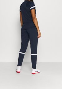 Námořnický sportovní outfit zahrnující přiléhavé tričko s krátkými rukávy a zúžené kalhoty s bílými pruhy jako akcent; doplněno bílými a červenými kopačkami.