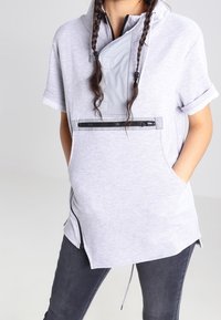 Light gray pullover hoodie with short sleeves, a funnel neck, zippered pocket, side zippers, and a loose fit. Textured fabric with a sporty design.