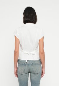 Λευκό μπλουζάκι με κοντά μανίκια, εφαρμοστή σχεδίαση, δέσιμο στη μέση και απαλή υφή. Φορεμένο με ανοιχτόχρωμο μπλε τζιν με ραφή στις πίσω τσέπες.