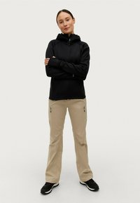 Zwarte rits hoodie met een capuchon, gecombineerd met beige cargobroeken met ritssluitingen, en zwarte sportieve schoenen. Eenvoudig, functioneel ontwerp.