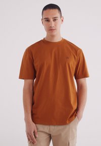 Korte mouwen bruine T-shirt van katoen, met een ronde hals en een klein logo op de borst. De pasvorm is casual en ontspannen.