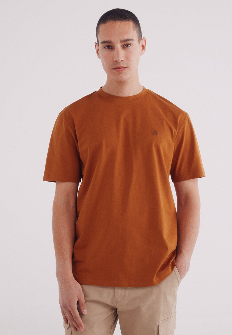 Korte mouwen bruine T-shirt van katoen, met een ronde hals en een klein logo op de borst. De pasvorm is casual en ontspannen.