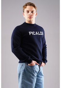 Navy sweatshirt with white "PICALDI" text, round neckline, and long sleeves, paired with light blue jeans. Fabric appears soft and casual.