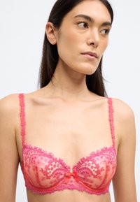 Ροζ δαντελένιο σουτιέν με διάφανους θύλακες, κεντήματα με λουλούδια και ρυθμιζόμενες τιράντες. Στο κέντρο έχει μια μικρή σατέν φιόγκο.