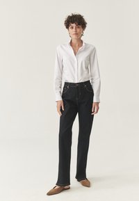 Pantaloni din denim de un albastru închis, cu croială dreaptă, asortați cu o cămașă albă cu nasturi. Prezintă cusături aurii și buzunare frontale.