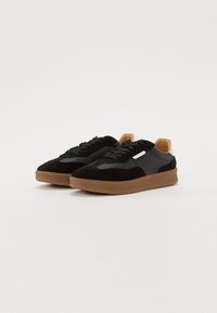 Schwarze Wildleder- und Synthetik-Sneaker mit einer braunen Gummisohle, ausgestattet mit grauen Schnürsenkeln und einem sandfarbenen Fersenakzent. Strahlt ein sportliches Design aus.