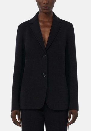Zwart op maat gemaakte blazer met inkepingrevers en twee knopen gedragen door persoon met een donkere huid tegen een effen achtergrond.