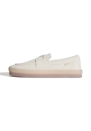 Off-white suède instapper met een dikke beige rubberen zool en een decoratieve band over de bovenkant.