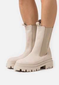 Beige Leder-Ankle-Boots mit elastischen Seitenpaneelen, einer stabilen Sohle mit tiefem Profil und einer glatten Oberfläche am Obermaterial.
