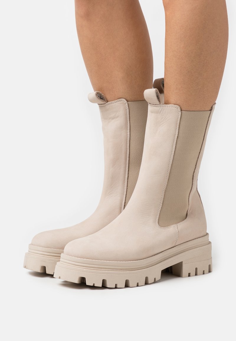 Beige Leder-Ankle-Boots mit elastischen Seitenpaneelen, einer stabilen Sohle mit tiefem Profil und einer glatten Oberfläche am Obermaterial.