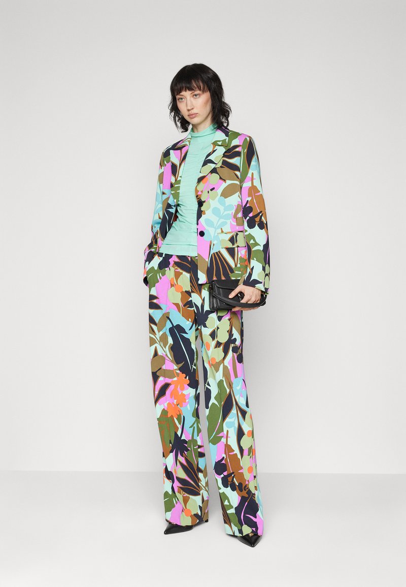 Garniturowy komplet w kwiatowy wzór w wielu kolorach, składający się z dopasowanej marynarki i spodni o szerokich nogawkach, zestawiony z miętową bluzką i elegancką czarną torebką.