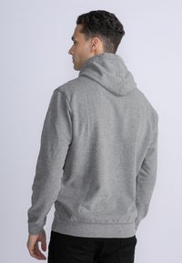 Sudadera gris con capucha y mangas largas, hecha de una tela suave. Presenta puños y cinturilla de canalé. Diseño simple, sin patrones ni acentos.