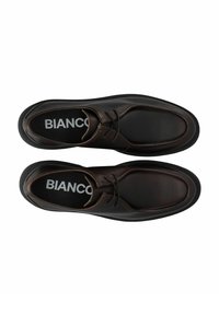 Chaussures en cuir marron avec une forme arrondie et une surface texturée. Elles disposent d'une semelle en caoutchouc noire et d'un système de laçage. Logo visible à l'intérieur.