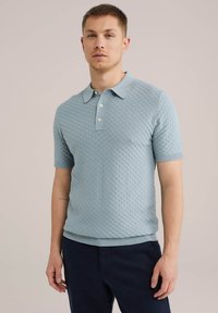 Svetlo modra polo majica s kratkimi rokavi, izdelana iz teksturirane pletenine, z ovratnikom in tremi belimi gumbi. Elastični manšeti in rob.