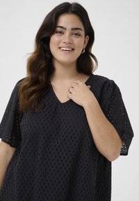 Black, loose-fitting blouse with a v-neckline, short puff sleeves, and textured eyelet pattern throughout. Soft fabric with a breathable design.