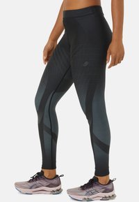 Leggings noirs texturés avec un design dégradé, arborant des motifs géométriques et une taille haute, assortis de chaussures de sport violettes.