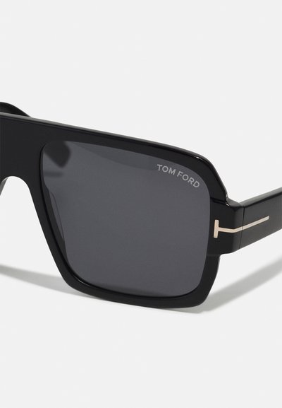 Occhiali da sole rettangolari neri con lenti scure. Presentano il logo silver "TOM FORD" e un accento minimalista silver sulla tempia. Montatura in plastica liscia.