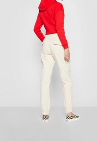 Béžové cargo kalhoty s elastickými manžetami, středně vysokým pasem, předními a zadními kapsami. Spárovány s jasně červenou mikinou a černobílými kostkovanými botami.