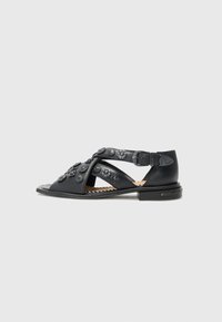 Black leather sandals featuring floral embellishments, open toe, and adjustable ankle strap on a low heel. Smooth texture with cut-out design.