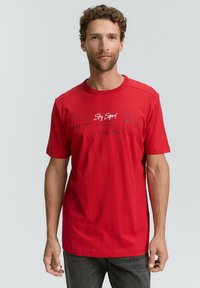 Rotes Baumwoll-T-Shirt mit kurzen Ärmeln, rundem Ausschnitt und bedrucktem Text in Weiß und Dunkelblau. Glatte Textur, lockere Passform.