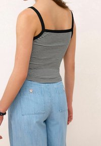 Débardeur rayé noir et blanc à fines bretelles, associé à un jean bleu clair taille haute avec des poches arrière boutonnées.