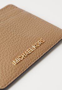 Rudas struktūruotas piniginės kortelių laikiklis su auksiniu "MICHAEL KORS" logotipu priekyje. Lygus juodas vidus su skyrių vietomis.
