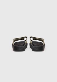 Et par olivengrønne sandaler med sorte strukturerte såler vist fra baksiden, med justerbare stropper over toppen.