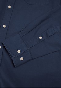 Marineblaue Hemdjacke mit langen Ärmeln, einer Brusttasche und hellen Knöpfen. Das Material hat eine glatte Textur.