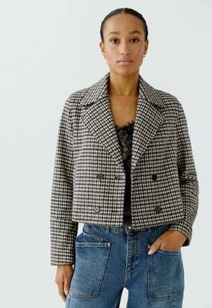 Cropped houndstooth jas in zwart en roomkleur met dubbelzijdige knopen, notch-kraag en gestructureerde silhoeet, gecombineerd met blauwe jeans.