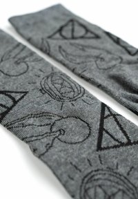 Calzini grigi con modelli neri di simboli, tra cui un triangolo con un cerchio, mani e disegni circolari, con una finitura a maglia testurizzata.