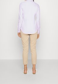 Camisa de manga larga lila claro con detalles de botones, combinada con pantalones ajustados color beige claro y sandalias de deslizar beige con la espalda descubierta.