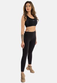 Svart sports BH og høyt liv leggings, med en myk tekstur og tettsittende design. Brune snøresko fullfører antrekket.