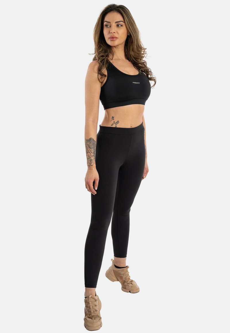 Svart sports BH og høyt liv leggings, med en myk tekstur og tettsittende design. Brune snøresko fullfører antrekket.