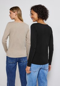 Långärmade toppar i beige och svart bomull, med rundad halsringing. Båda är kombinerade med denimjeans och har en avslappnad passform.