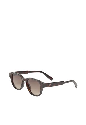 Lunettes de soleil rondes écaille foncée avec des verres marron dégradés et des branches épaisses et incurvées, montrées légèrement inclinées sur fond blanc.